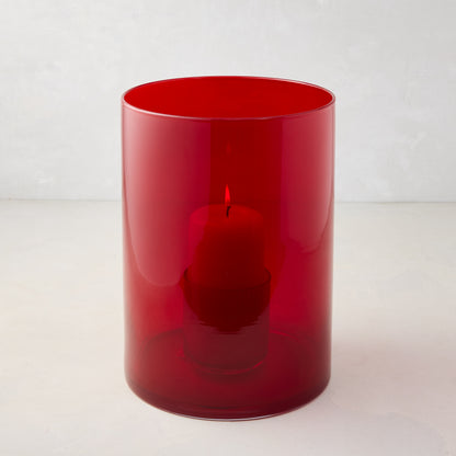 Medium red glass hurricane with a lit red pillar candle inside.