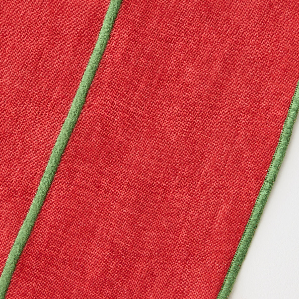 Red linen table runner with green embroidered trim and contrast stitching detail.