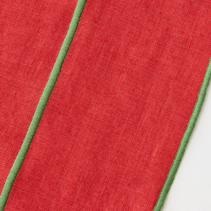 Red linen table runner with green embroidered trim and contrast stitching detail.