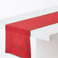 Red linen table runner with green embroidered border detail draped over a white table.