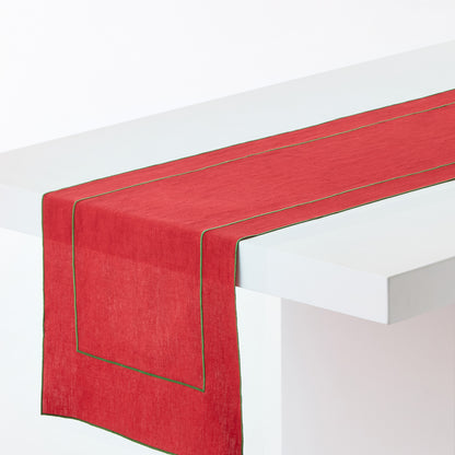 Red linen table runner with green embroidered border detail draped over a white table.