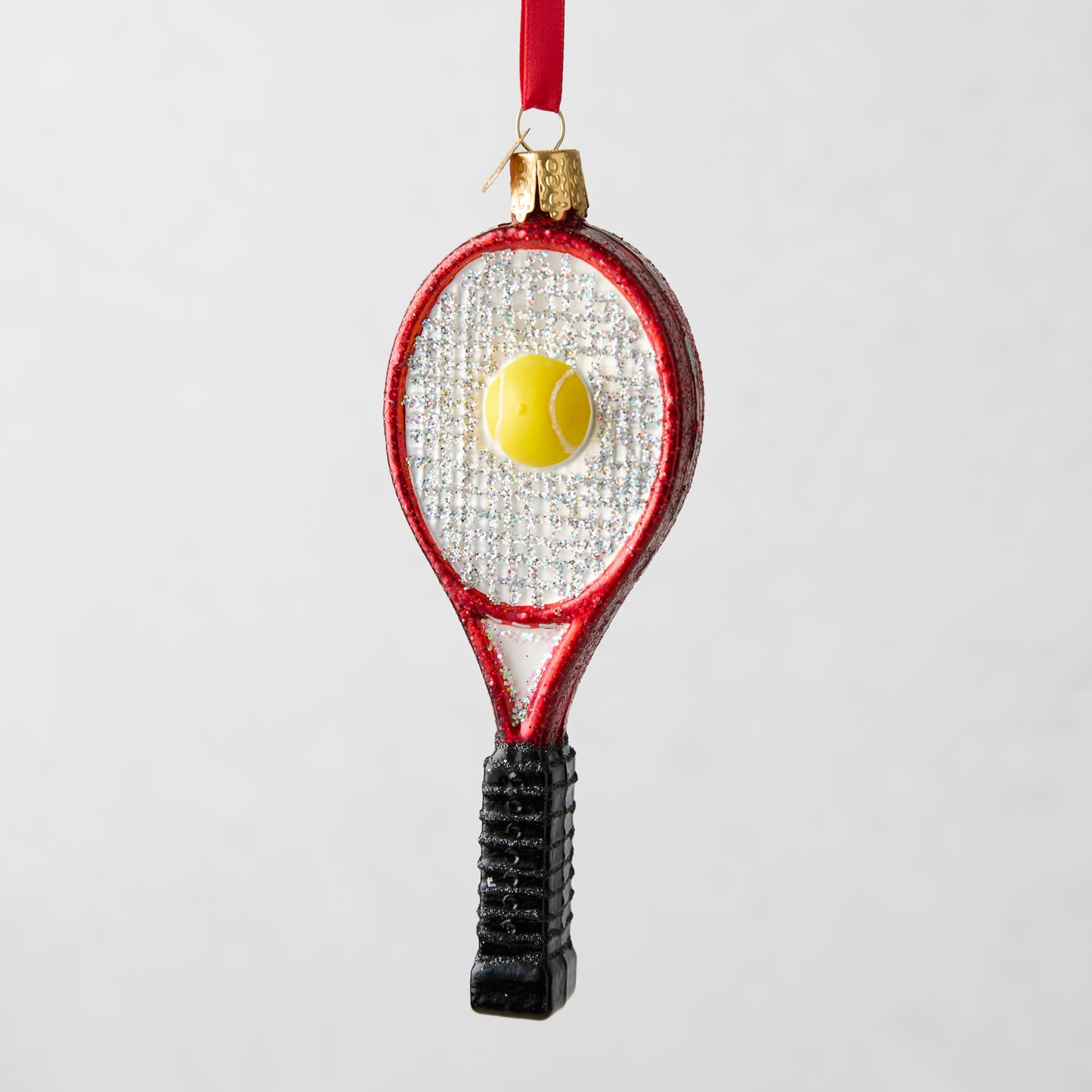 Red glitter tennis racquet Christmas ornament with a yellow tennis ball, black handle, and red ribbon.