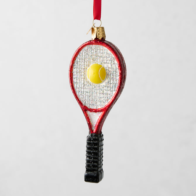 Red glitter tennis racquet Christmas ornament with a yellow tennis ball, black handle, and red ribbon.