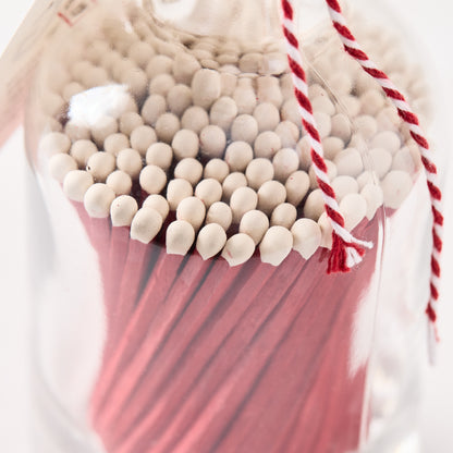 Glass bottle of oversized red matches with white tips, tied with red and white twine.