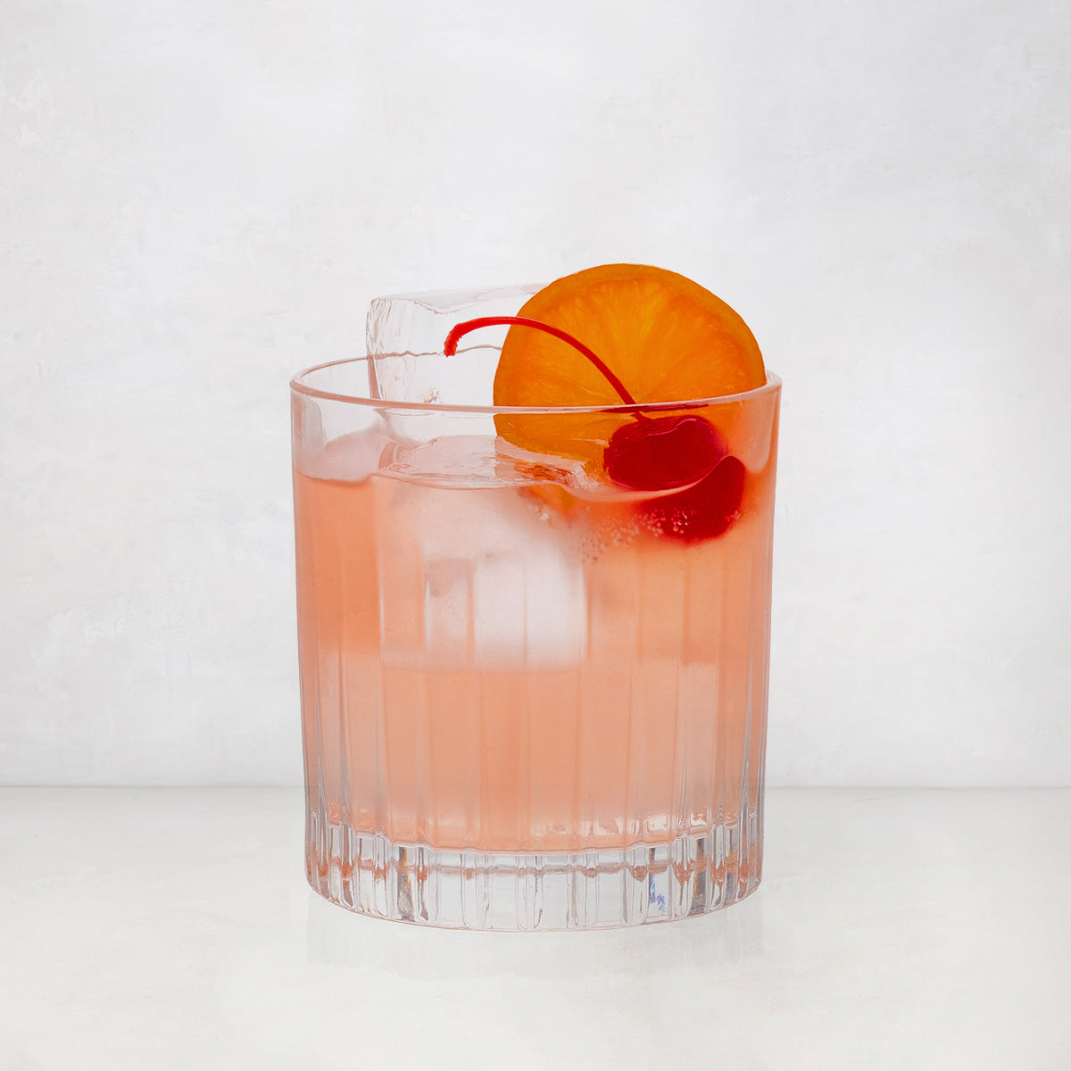 Regent Eco-Crystal Double Old-Fashioned Glass with a pink cocktail, ice, orange slice, and cherry.