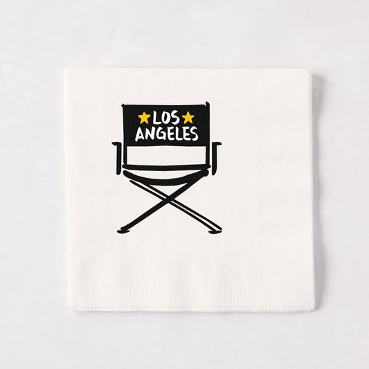 White 5.5-inch 3-ply paper cocktail napkin featuring a black hand-drawn director's chair illustration with Los Angeles text.