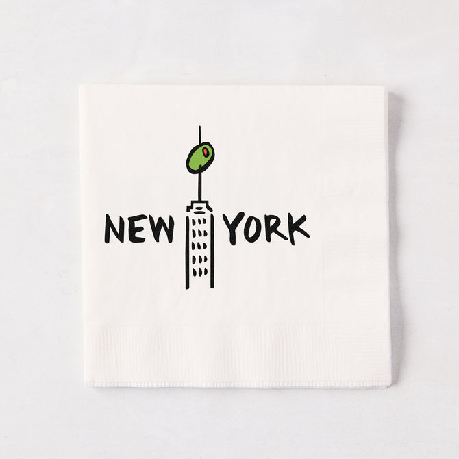 White 5.5-inch 3-ply paper cocktail napkin with a black New York skyscraper illustration topped with a green olive.