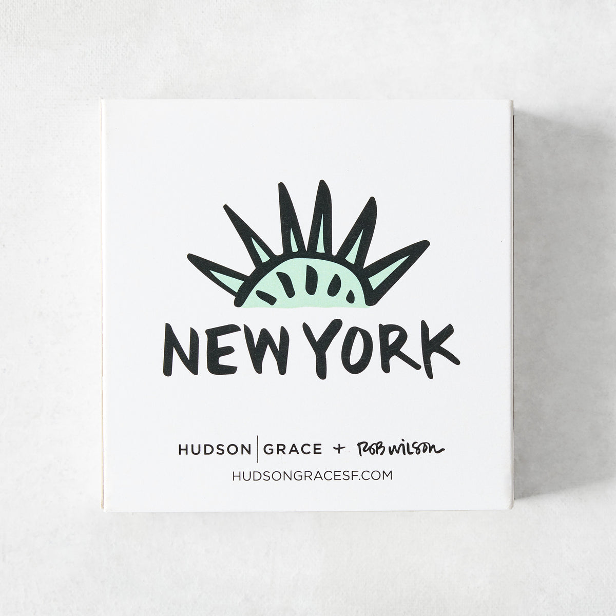 White square matchbox featuring a mint green Statue of Liberty crown illustration and New York text by Rob Wilson.