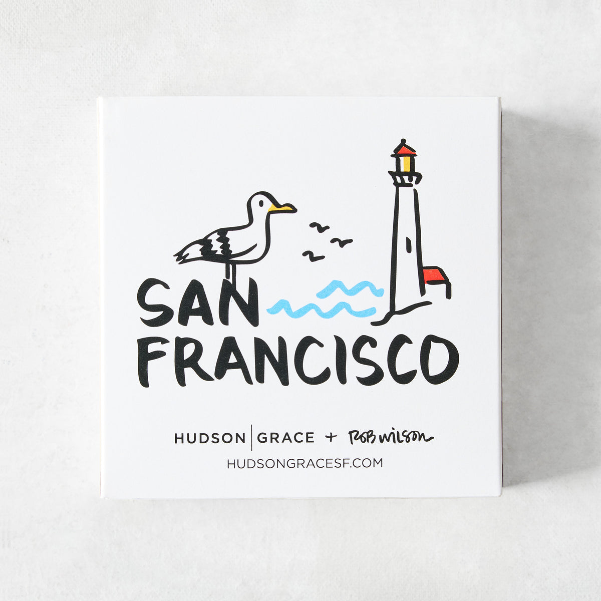 White square matchbox featuring a San Francisco illustration by Rob Wilson with a seagull, lighthouse, and blue waves.