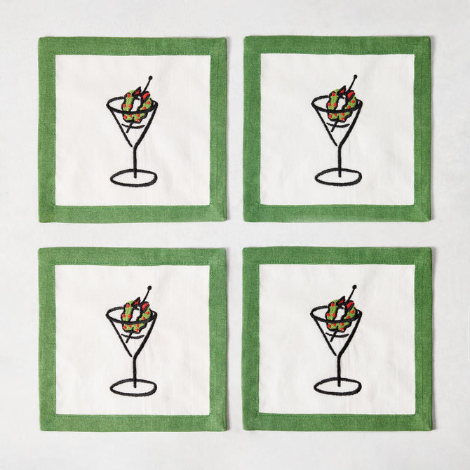 Set of four white linen coasters with green borders and embroidered martini glass illustrations with wreath garnishes.