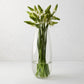 Tall, slender clear mouth-blown glass Robert Vase with green and white flowers.