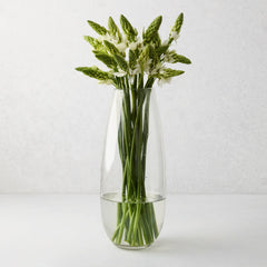 Tall, slender clear mouth-blown glass Robert Vase with green and white flowers.