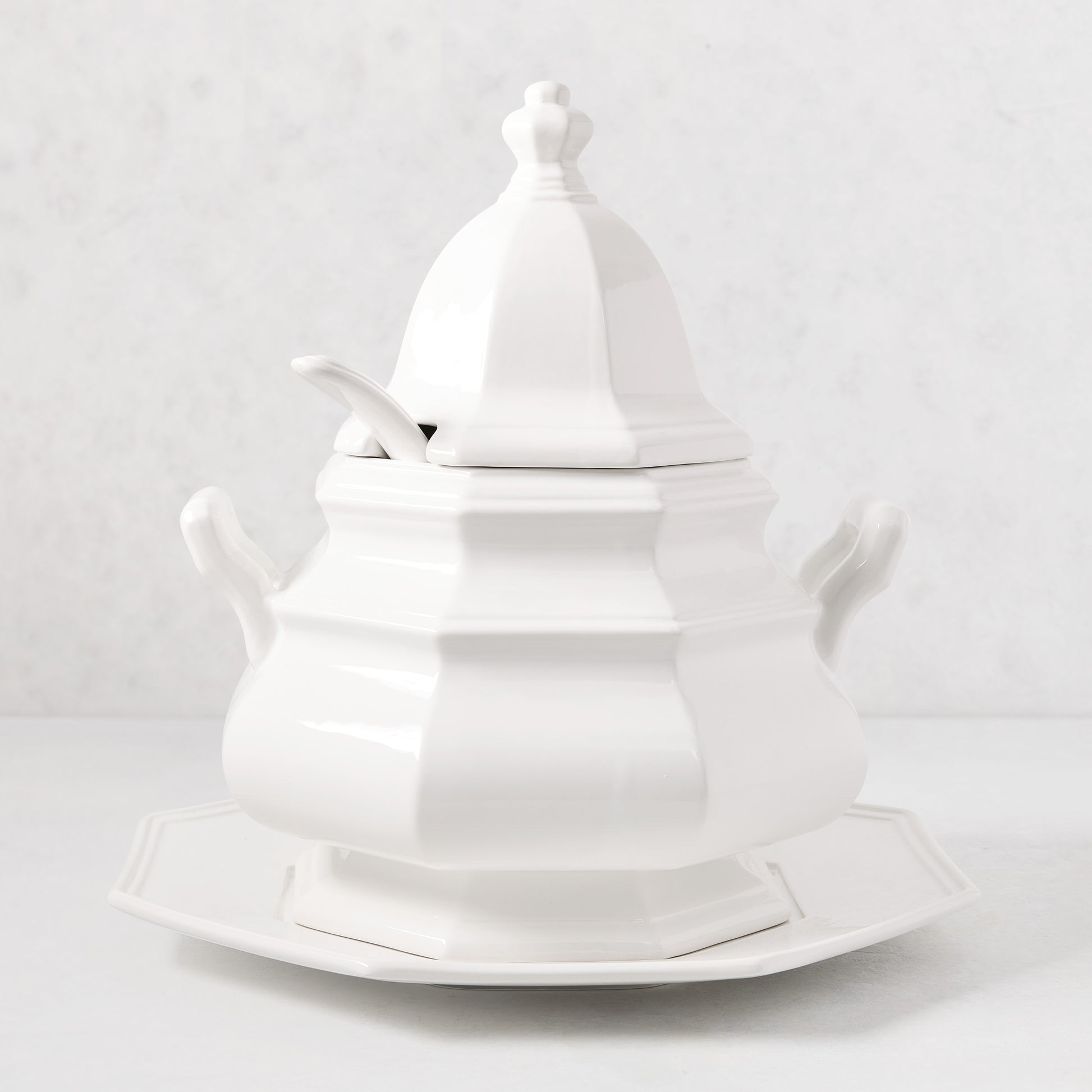 White ceramic Roma soup tureen with lid, spoon notch, handles, and matching octagonal base.