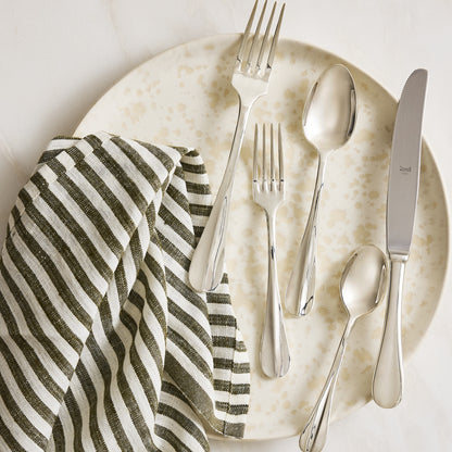 Roma Hotel 5-piece silverplate flatware set with a modern Neo-Baroque design on a speckled plate with a striped napkin.