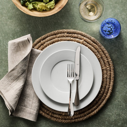 Roma Hotel silverplate table fork and knife set on white plates with a linen napkin and woven placemat.