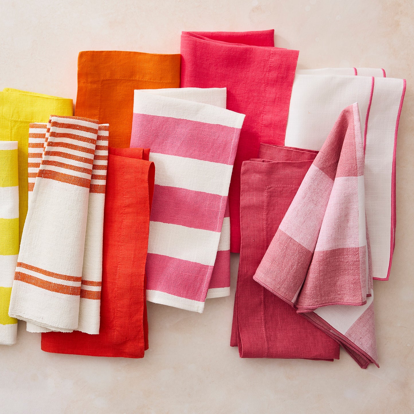 Collection of Rosy HG hand-dyed linen napkins in solid pink, orange, yellow, and striped patterns.