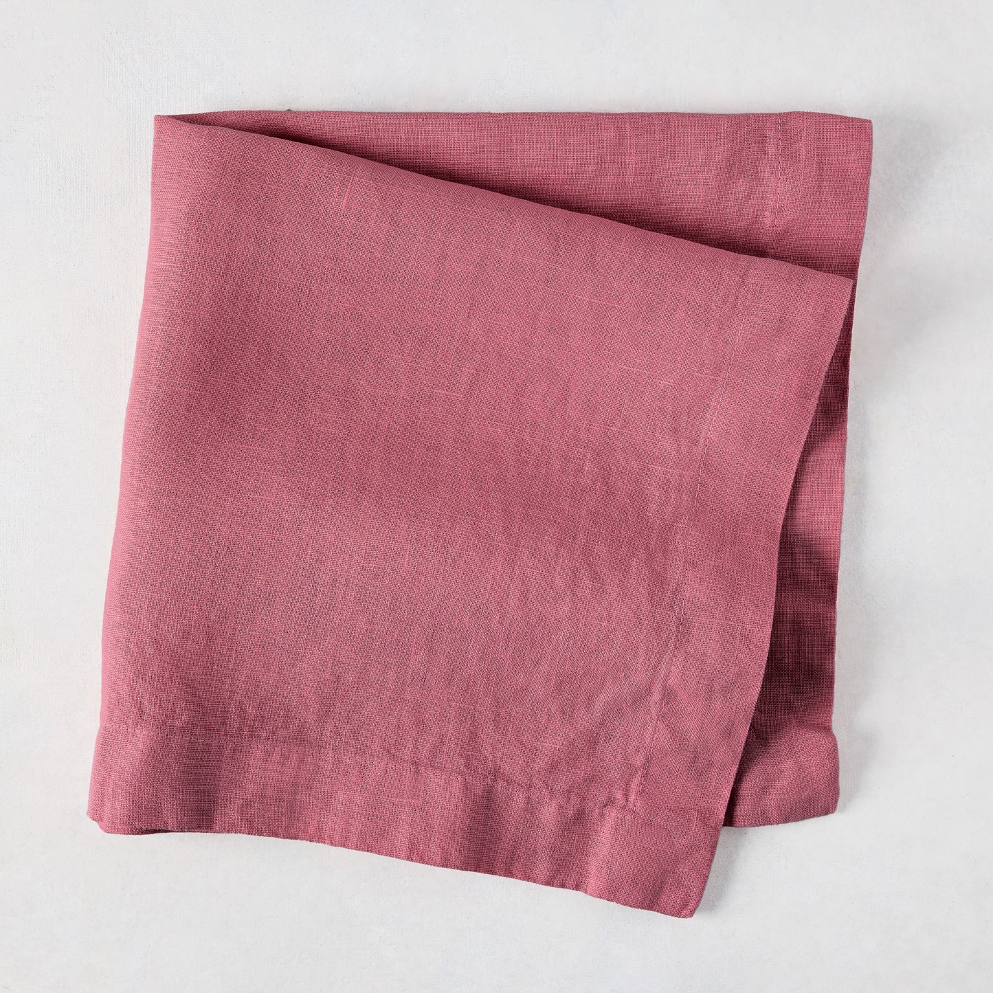 Rosy HG hand-dyed 22" square linen napkin, folded on a white surface.