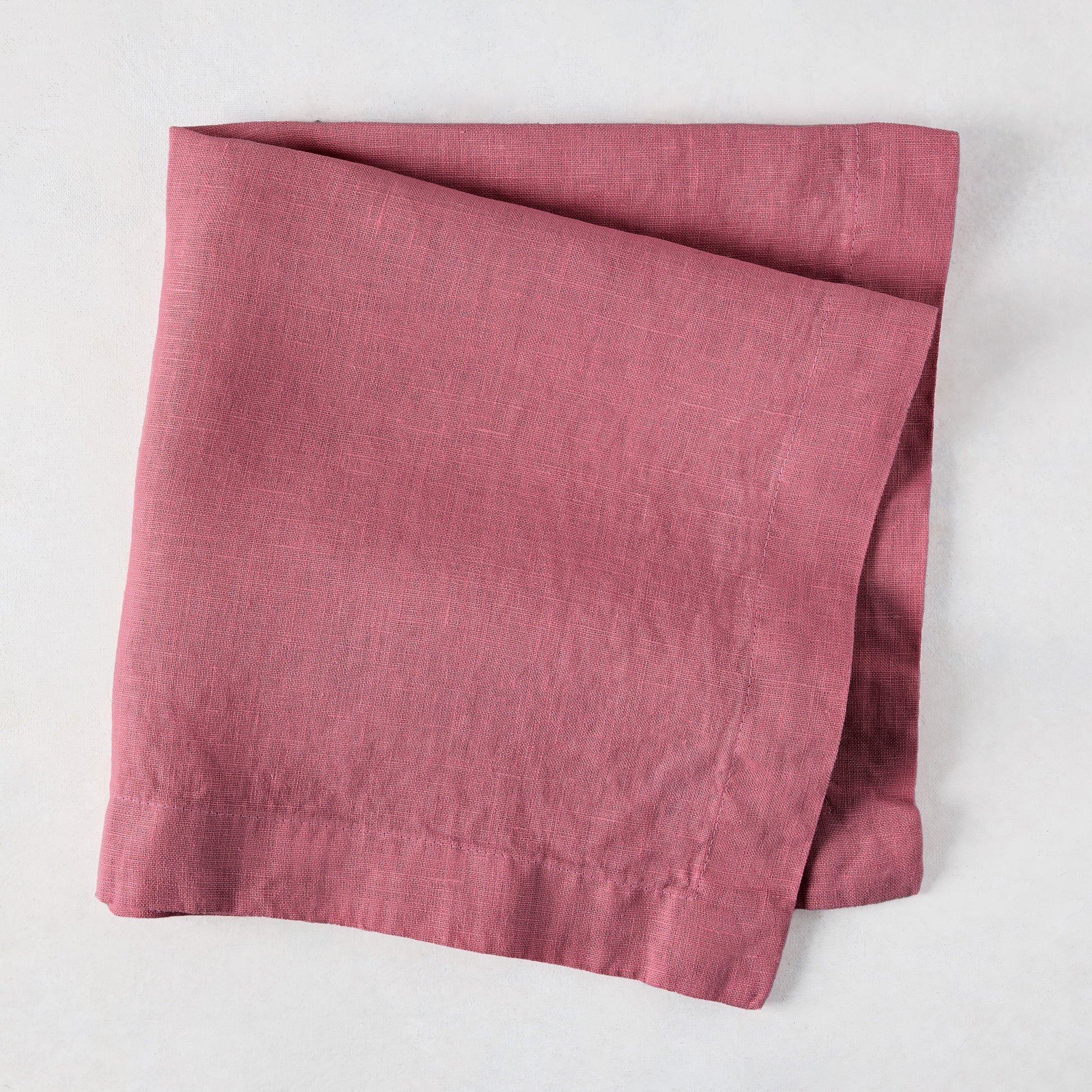 Rosy HG hand-dyed 22" square linen napkin, folded on a white surface.