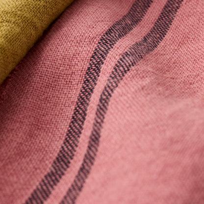 Rosy pink French linen tea towel with dark striped pattern, folded with a green fabric.