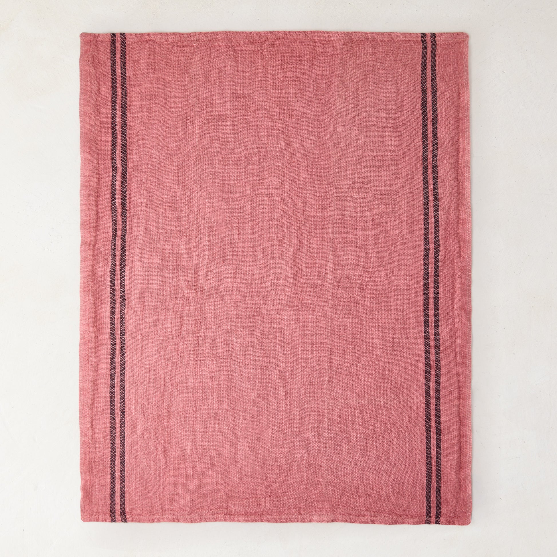 Rosy pink French linen tea towel with dark vertical stripes on each side.