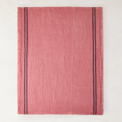 Rosy pink French linen tea towel with dark vertical stripes on each side.