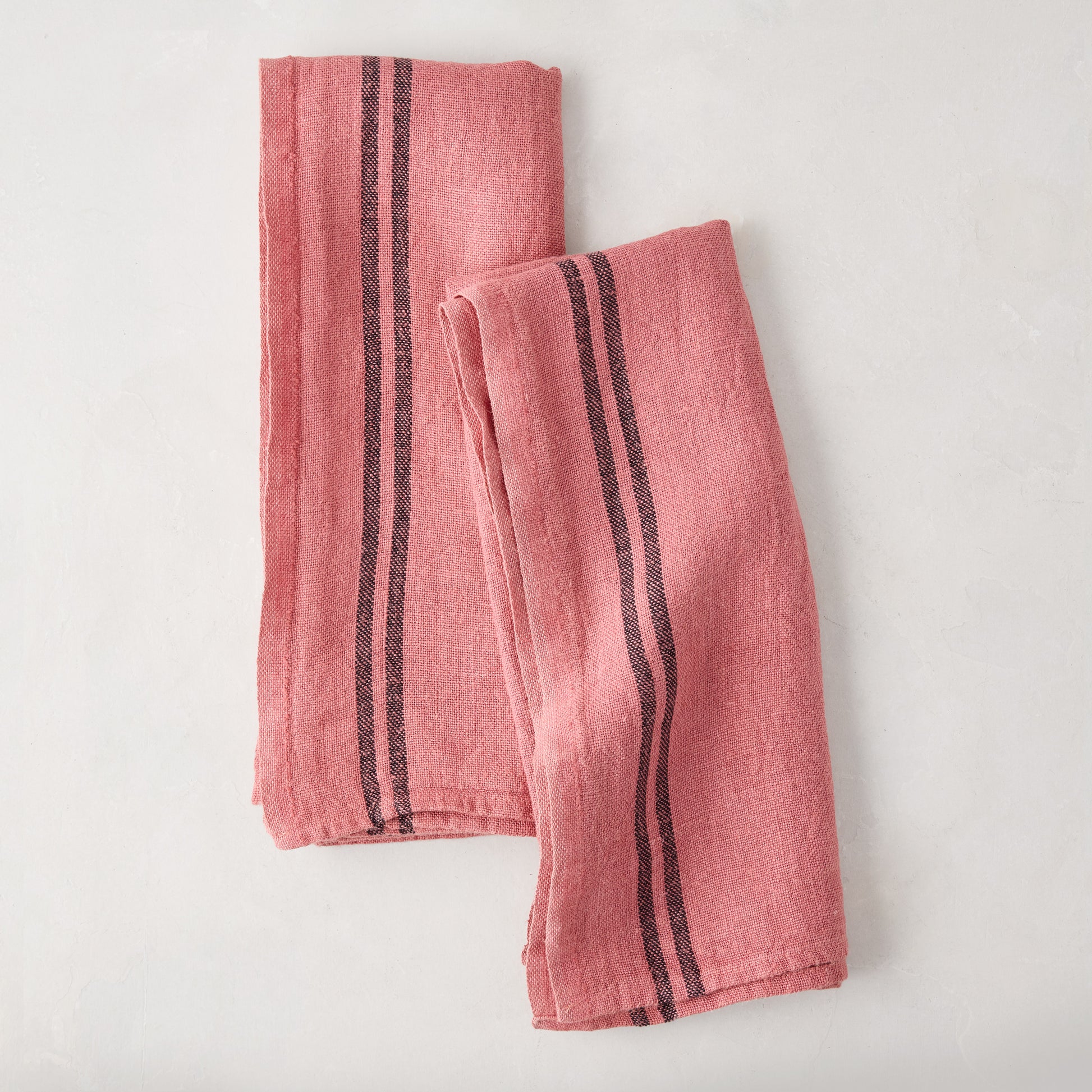 Set of 2 rosy pink French linen tea towels with black stripes, folded on a white surface.