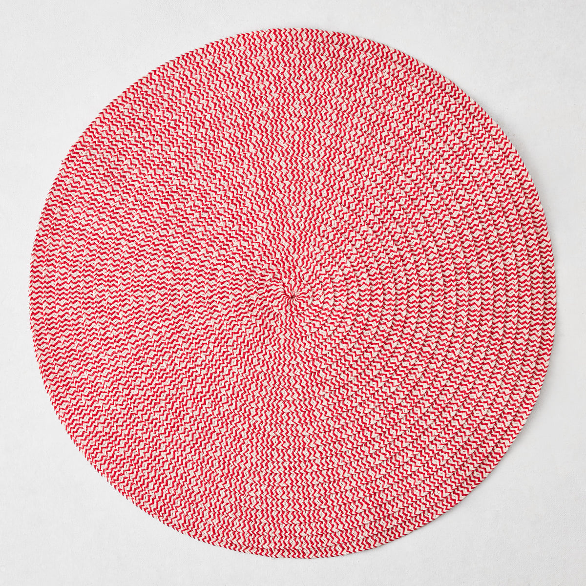 Round red and white tweed placemat with a woven spiral pattern on a white background.