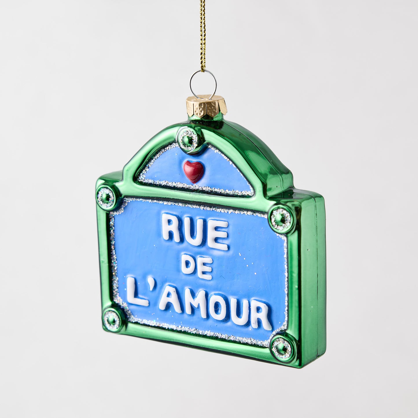 Rue De L'Amour street sign Christmas ornament in blue and green glass with glitter accents and a small red heart.