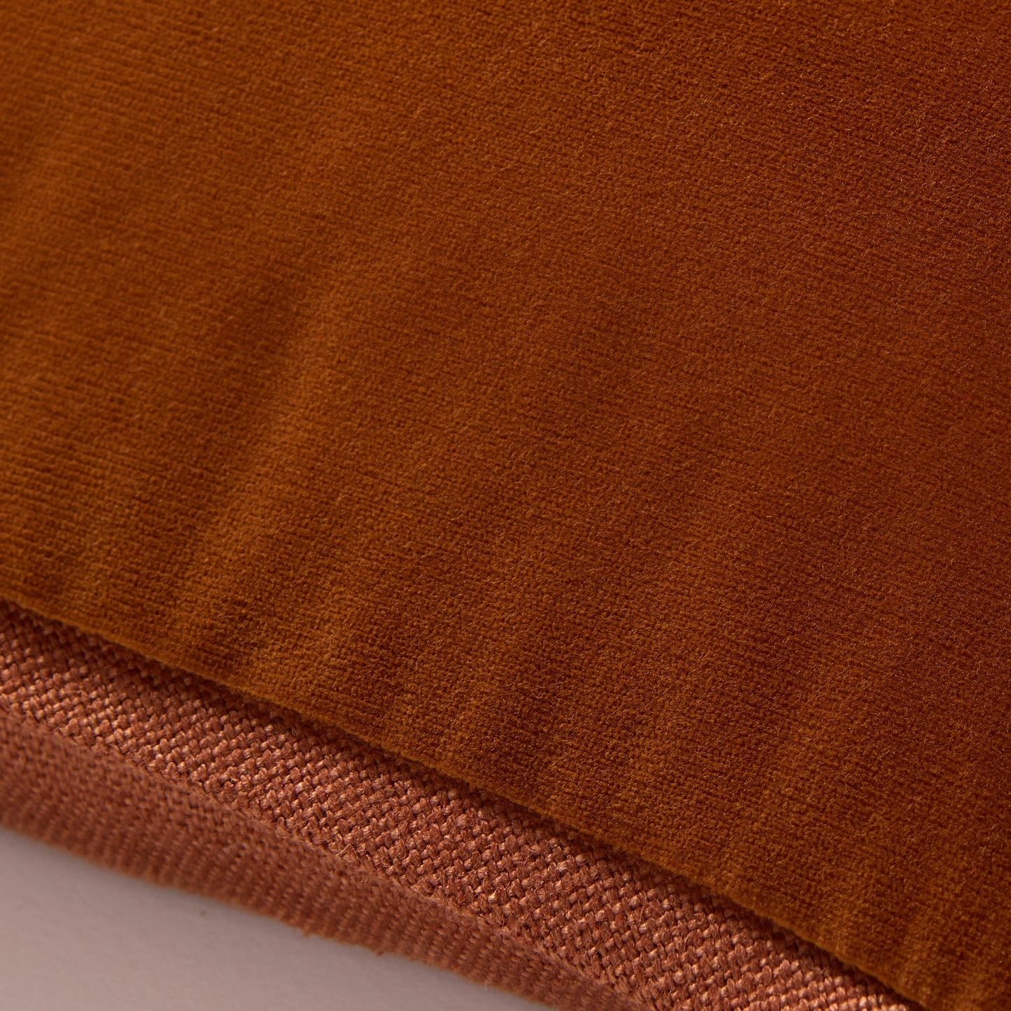 Close-up of a rust orange reversible lumbar pillow, showing velvet and linen textures.