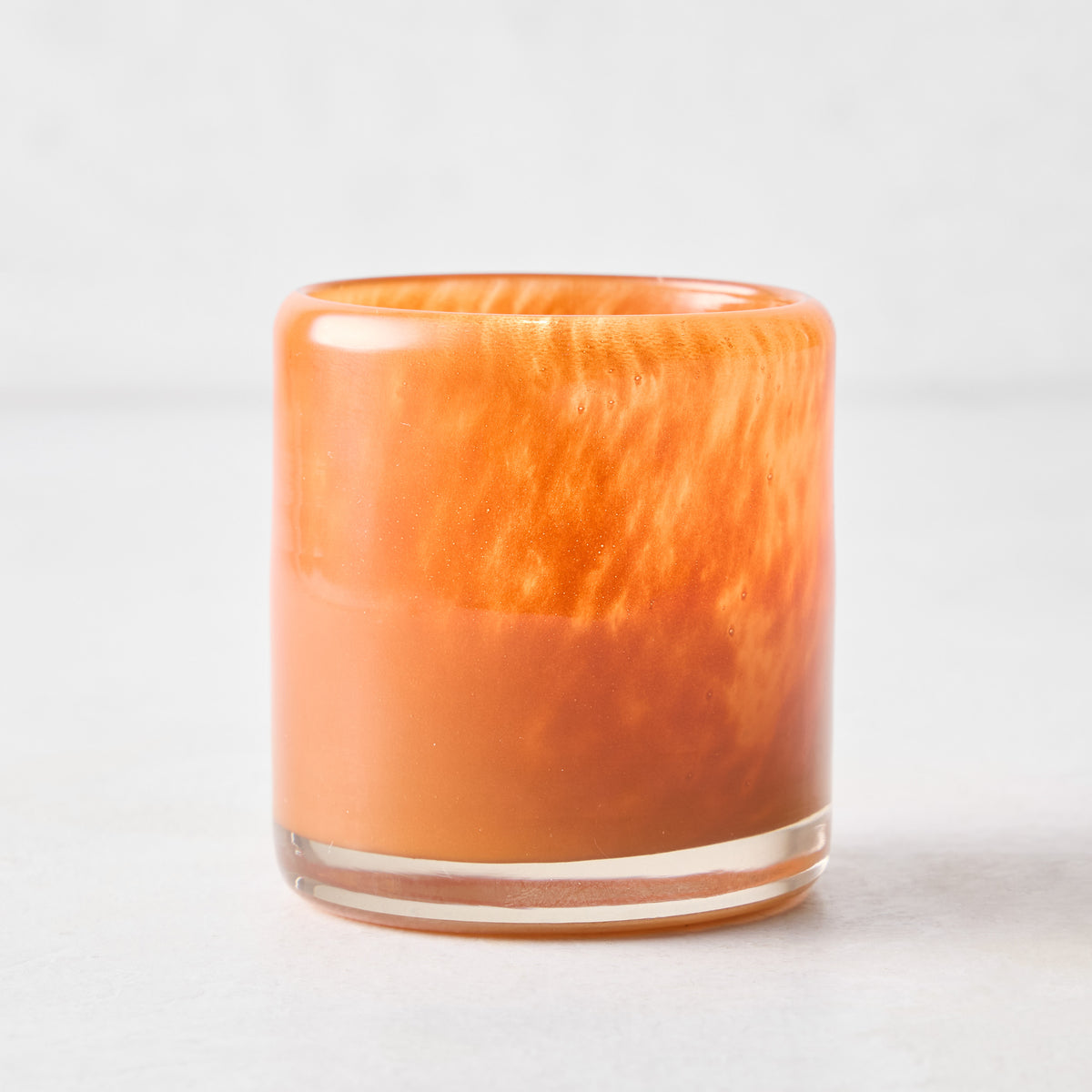 Small mouth-blown rust red glass votive candle holder with a thick base and translucent, marbled finish.