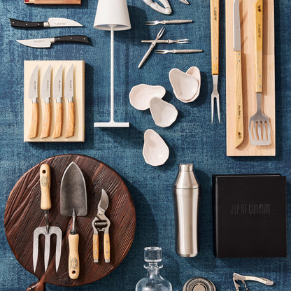 Dark brown, round, footed wood serving board with handle, garden tools, and kitchen utensils on a blue background.