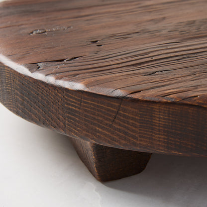 Dark brown, round, footed Saddle Wood serving board with visible wood grain and texture.