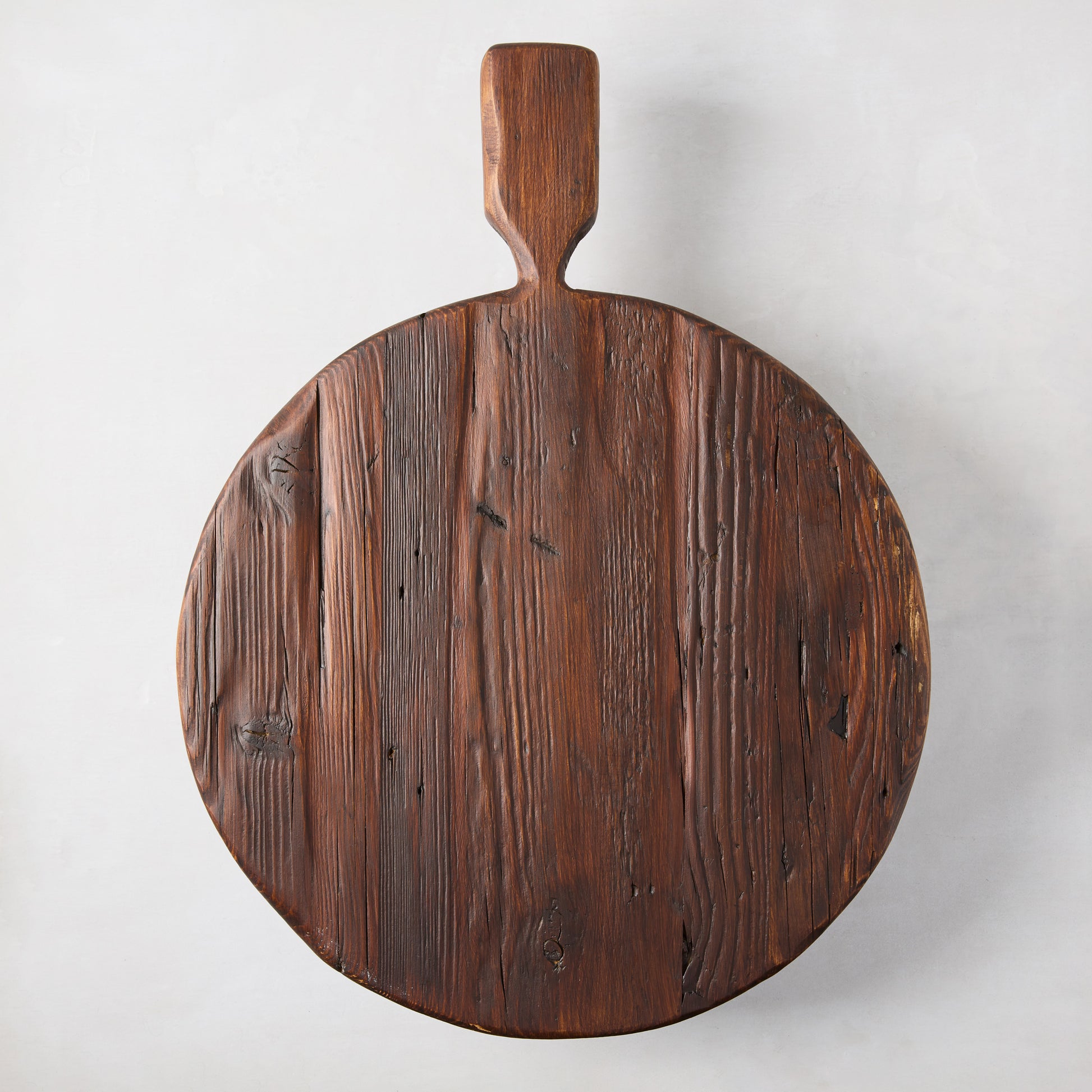 Round, dark brown, rustic European pine wood serving board with handle and footed design.