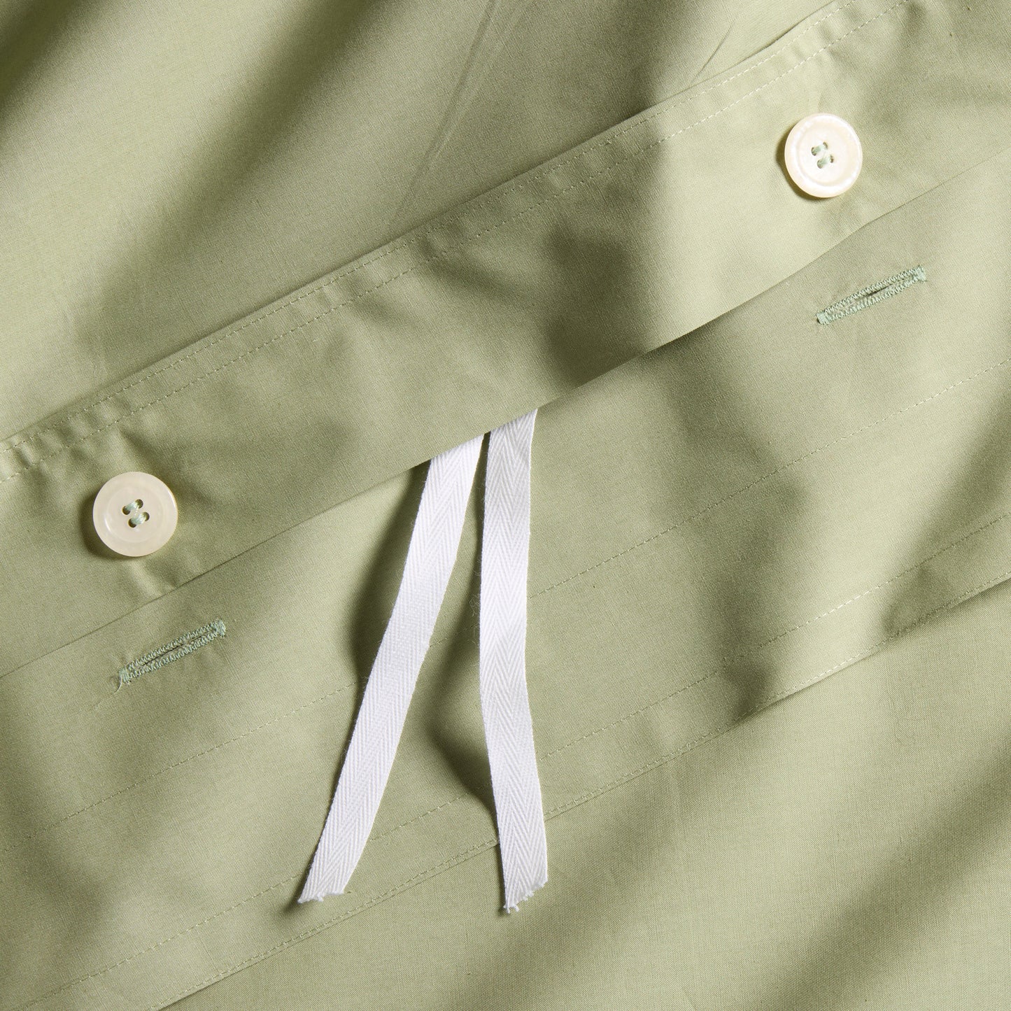 Close-up of a sage green Italian percale duvet cover with white button closures and interior ties.