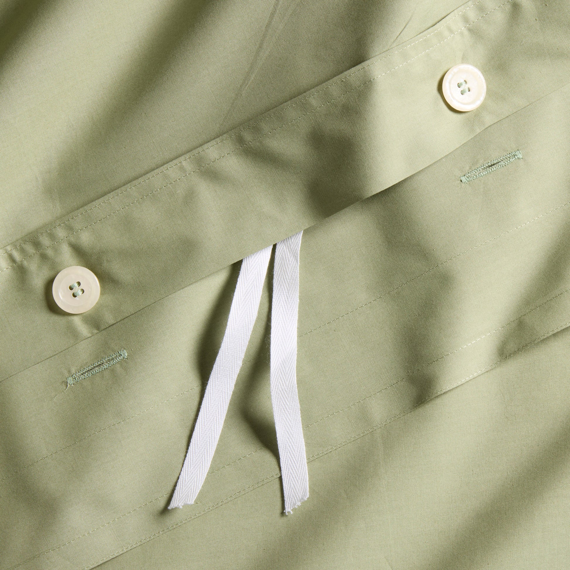 Close-up of a sage green Italian percale duvet cover with white button closures and interior ties.