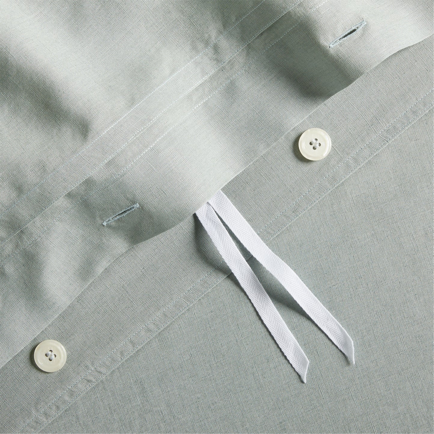 Close-up of sage green washed linen duvet cover with hidden-button closure, white buttons, and corner ties.