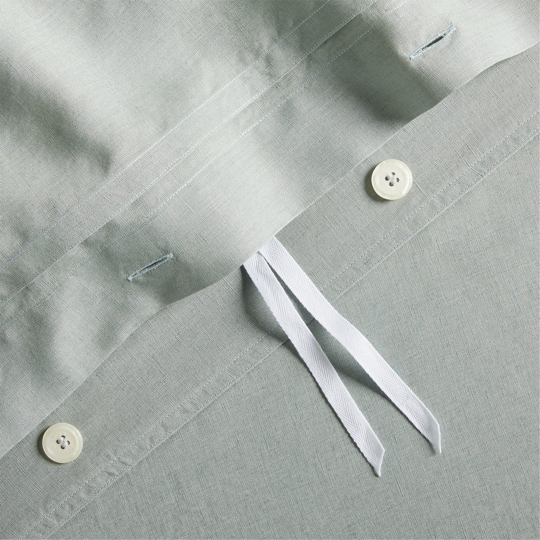 Close-up of sage green washed linen duvet cover with hidden-button closure, white buttons, and corner ties.