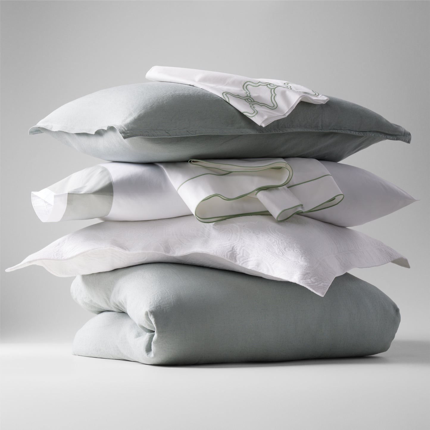 Stacked sage green washed linen duvet cover, pillows, and white embroidered shams.