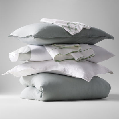 Stacked sage green washed linen duvet cover, pillows, and white embroidered shams.