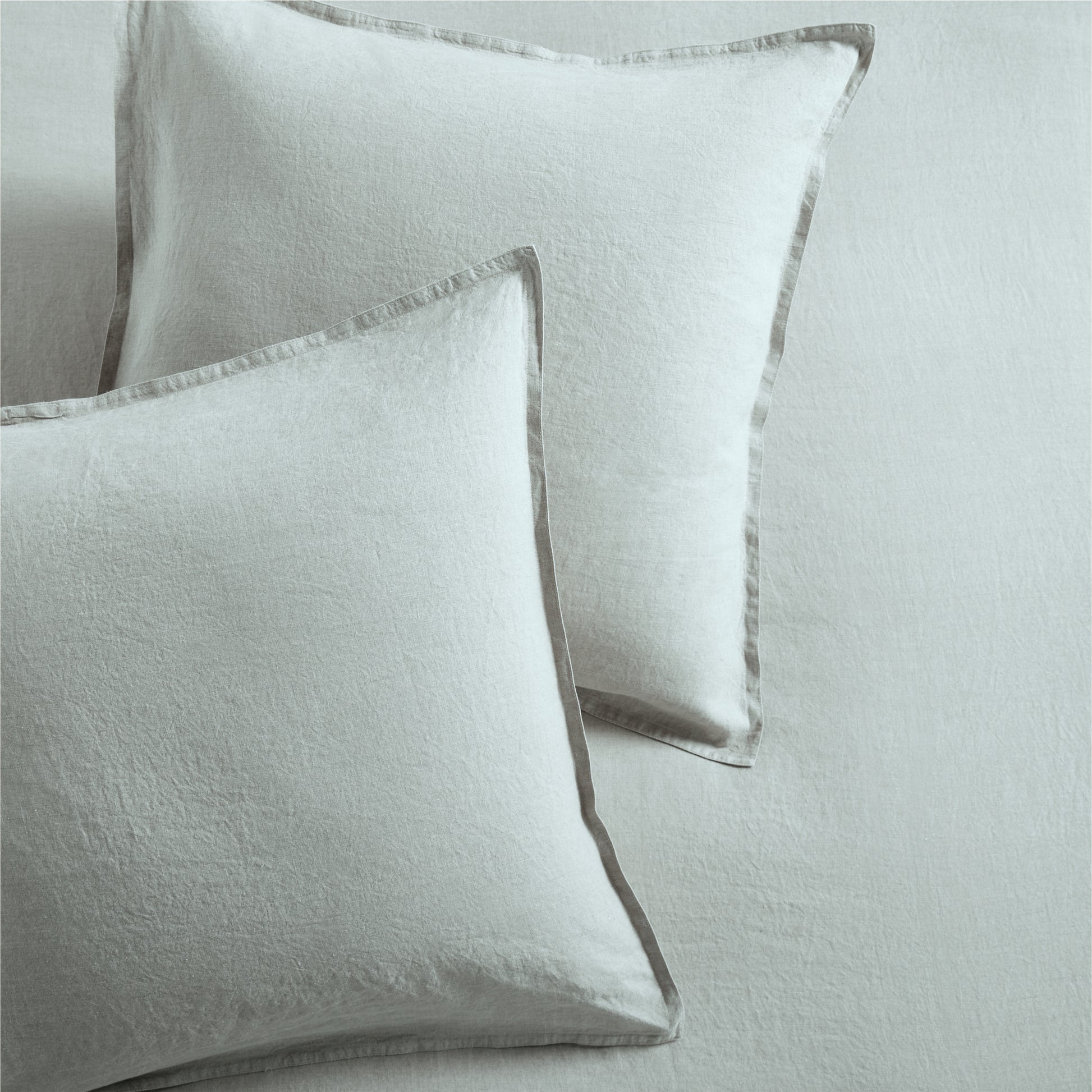 Two sage green washed linen pillow shams with 2" flange and double-needle stitching.