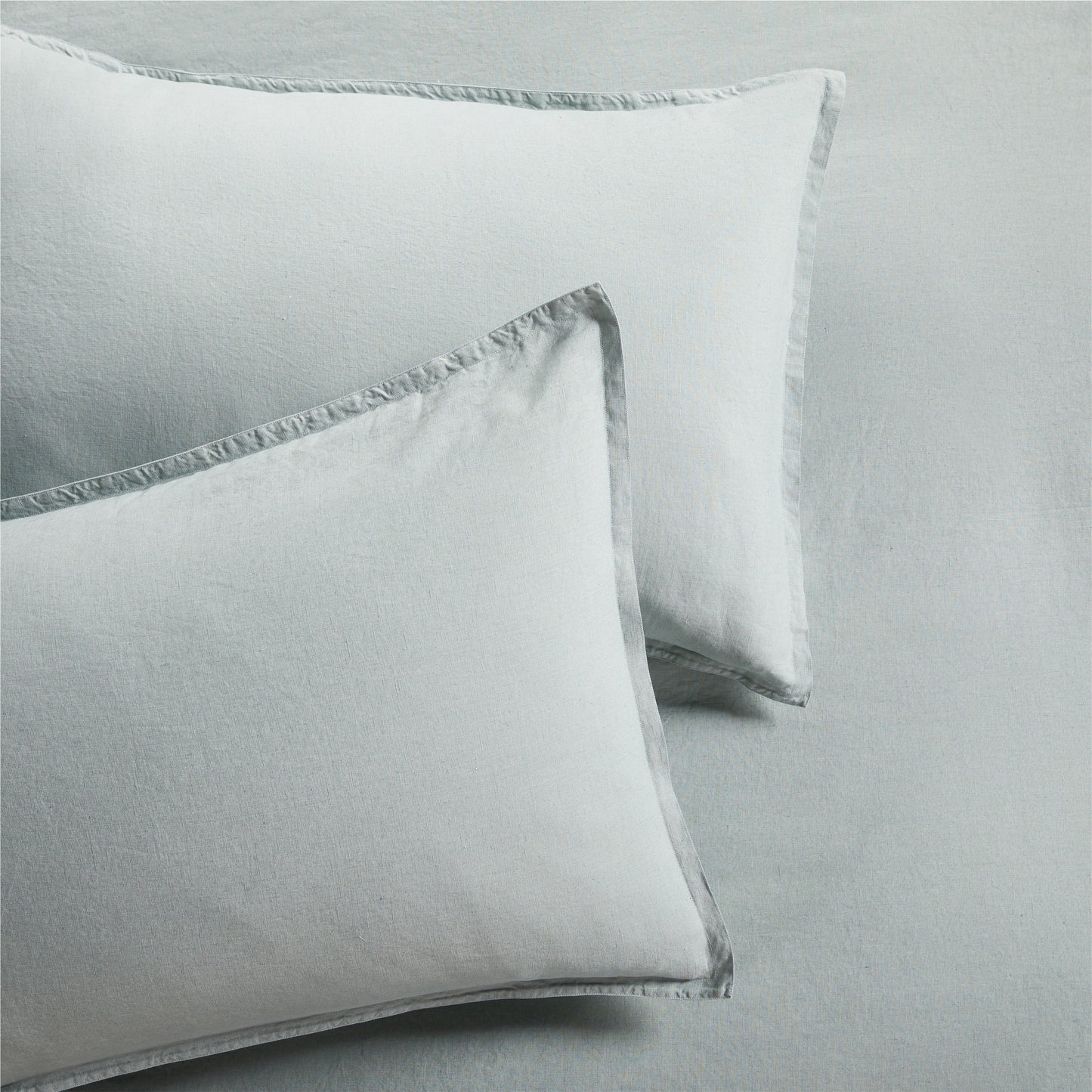 Two sage green washed linen pillow shams with a 2" flange and double-needle stitching.