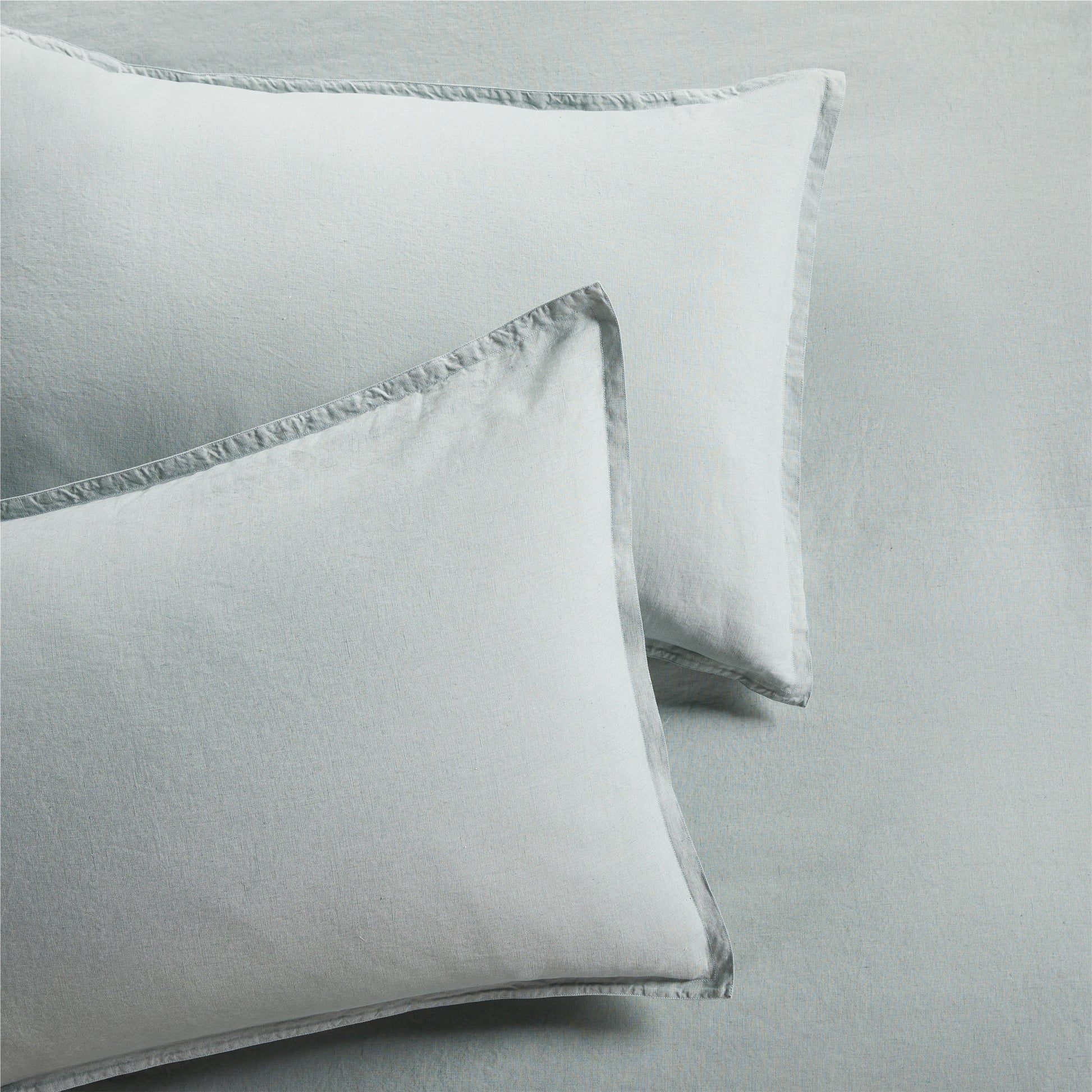 Two sage green washed linen pillow shams with a 2" flange and double-needle stitching.