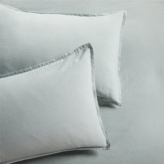 Two sage green washed linen pillow shams with a 2" flange and double-needle stitching.