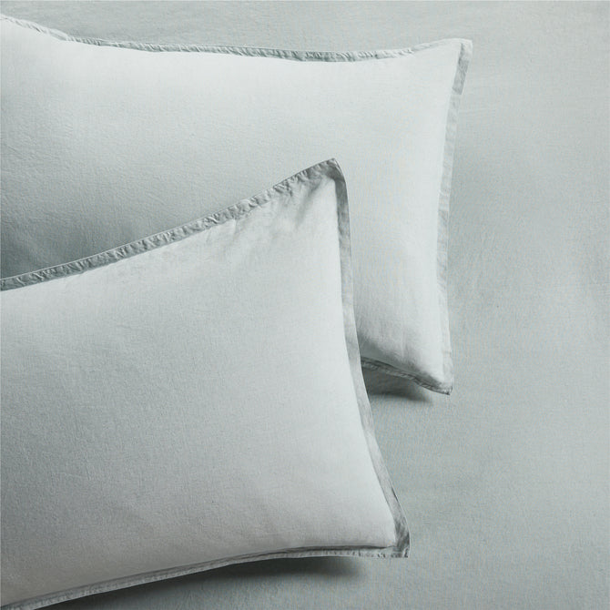 Two sage green washed linen pillow shams with a 2" flange and double-needle stitching.