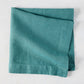 Sage HG Signature hand-dyed linen napkin, folded, showing earthy teal color and natural texture.