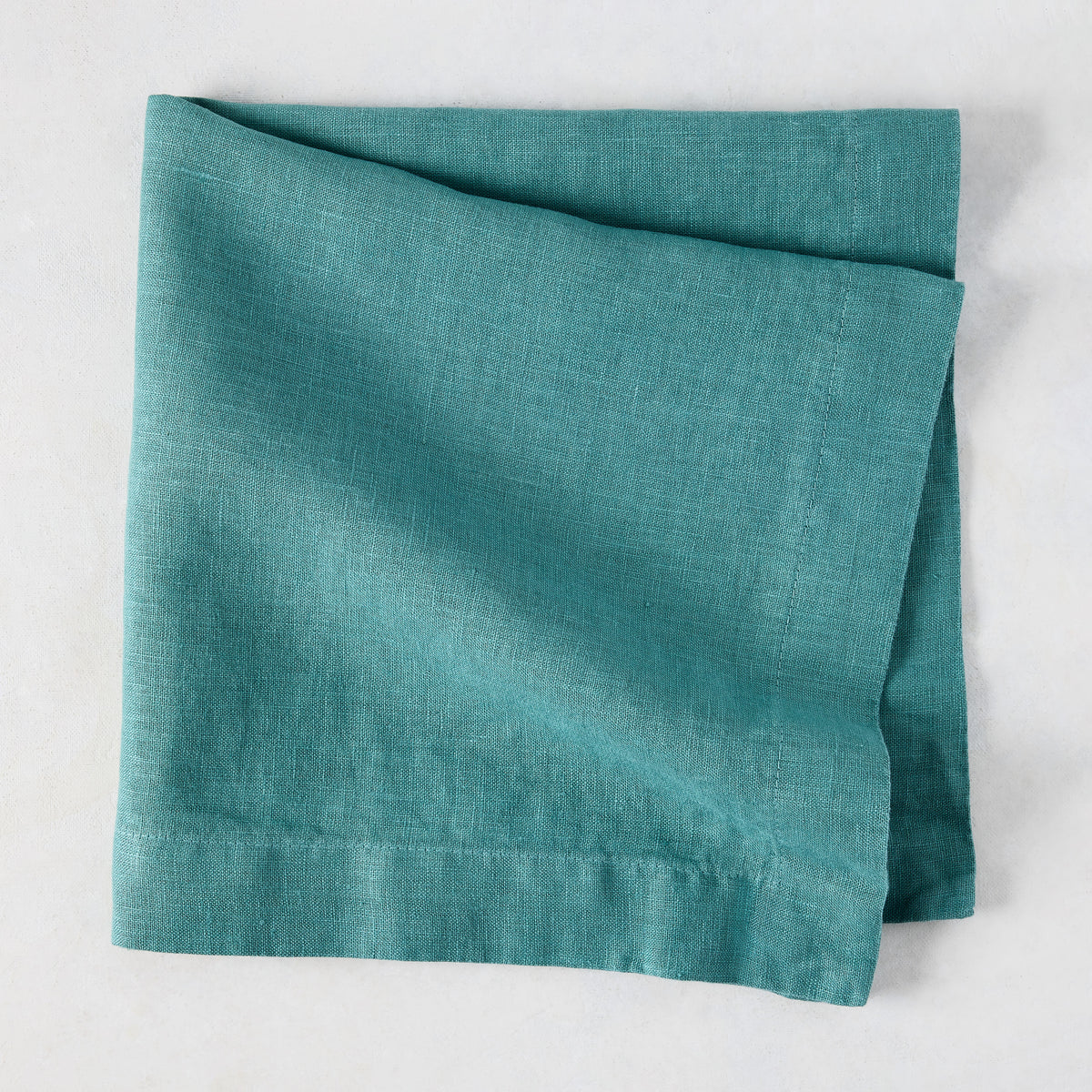Sage HG Signature hand-dyed linen napkin, folded, showing earthy teal color and natural texture.