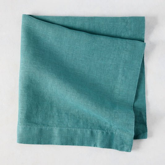 Sage HG Signature hand-dyed linen napkin, folded, showing earthy teal color and natural texture.