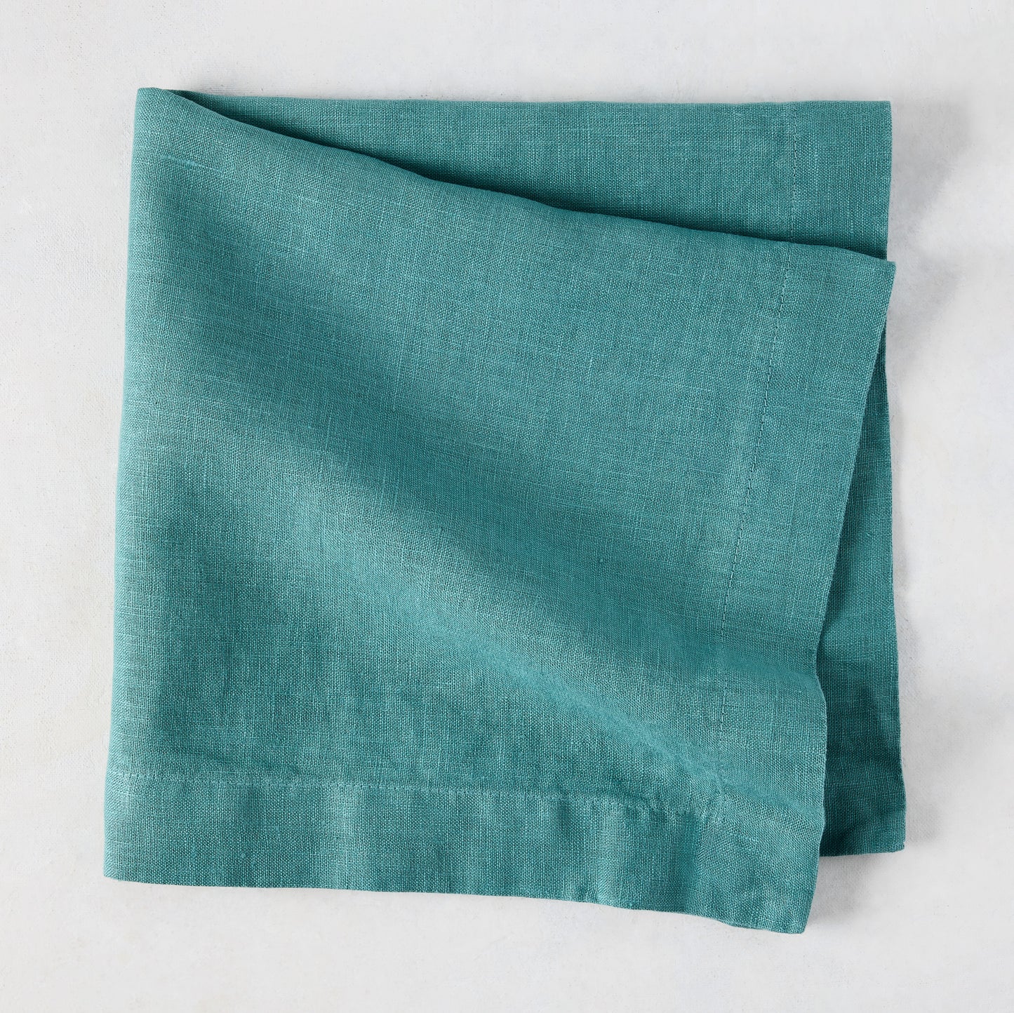 Sage HG Signature hand-dyed linen napkin, folded, showing earthy teal color and natural texture.