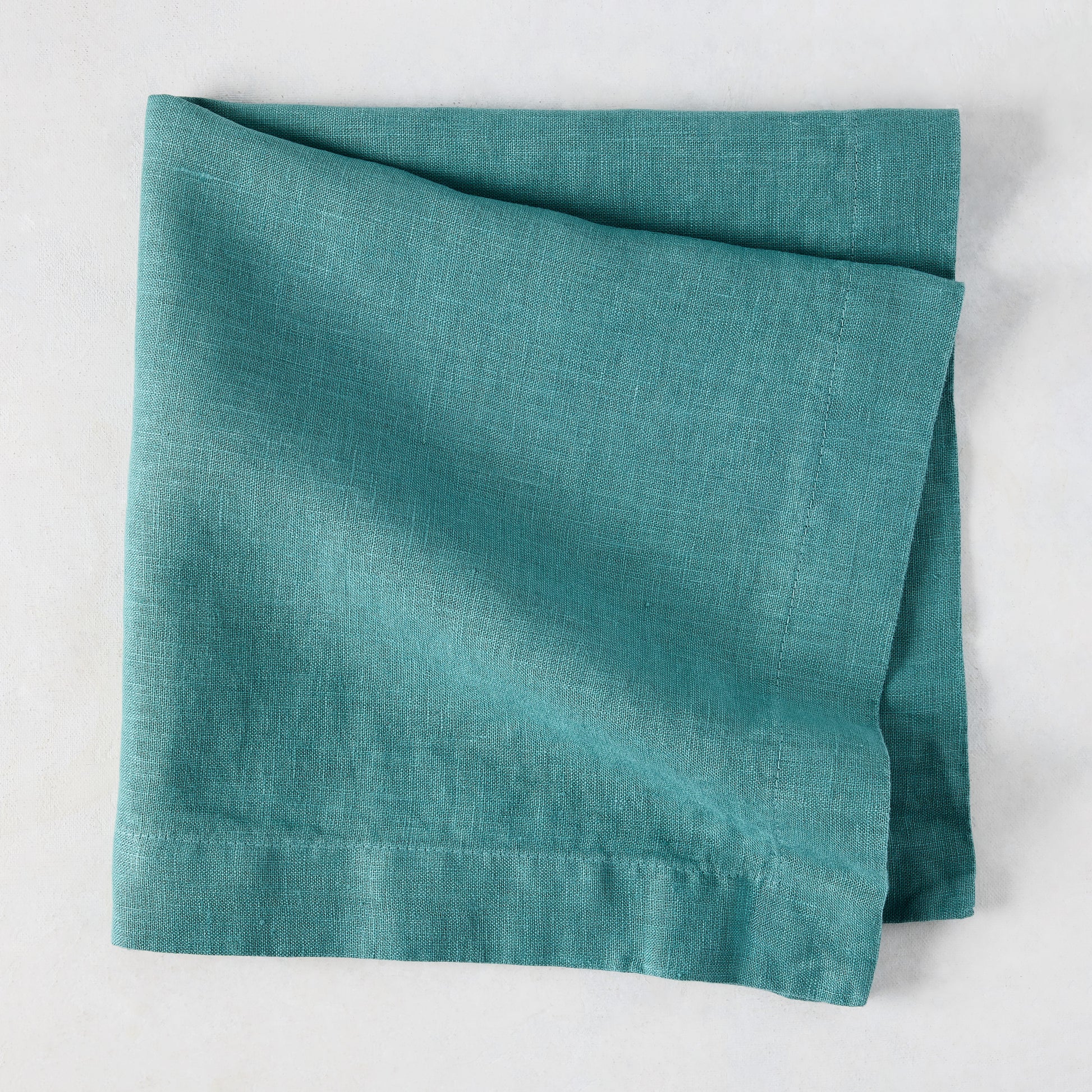 Sage HG Signature hand-dyed linen napkin, folded, showing earthy teal color and natural texture.