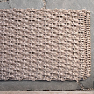 Handwoven sand and charcoal rope doormat with a tight weave, shown on a stone surface.